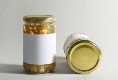 Glass jars with pickled baby corn on white background