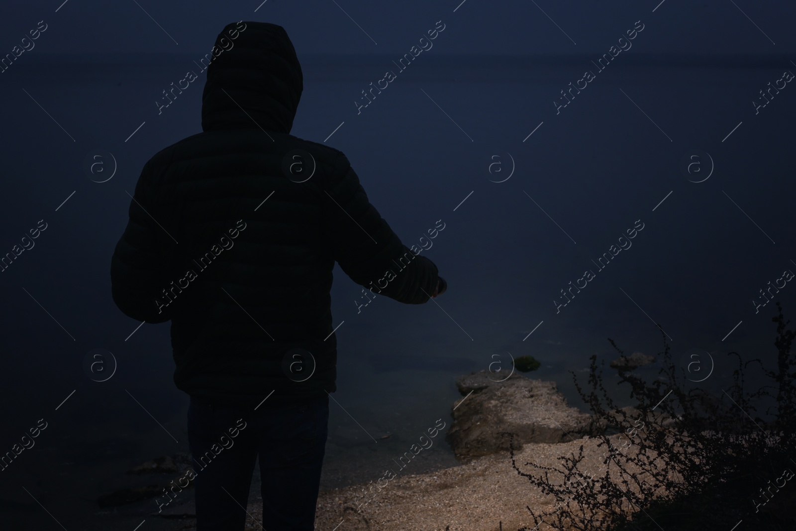 Photo of Man with flashlight walking near river in evening