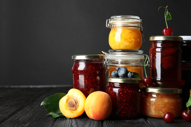 Photo of Jars with different jams and fresh fruits on black wooden table
