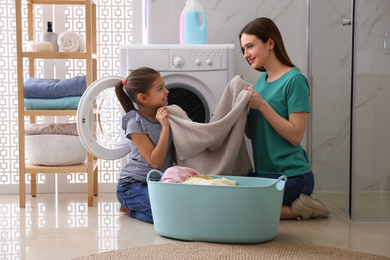 Mother and little daughter with clean laundry in bathroom