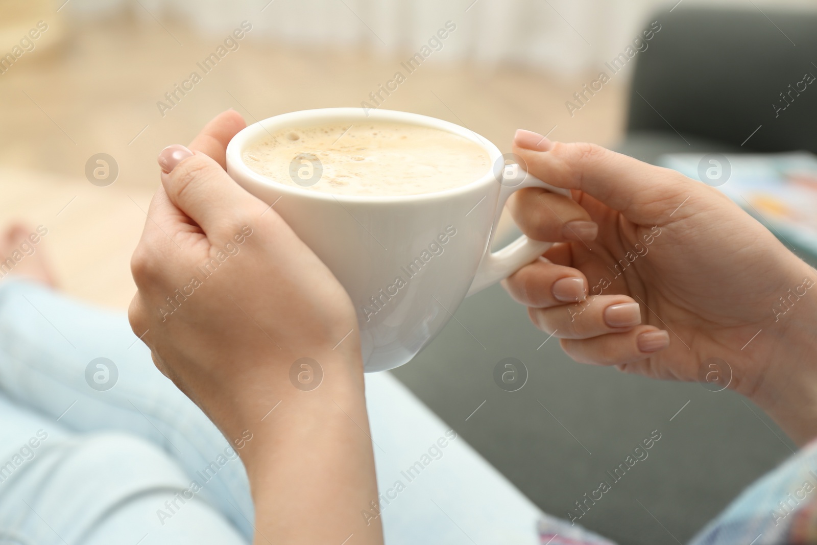 Photo of Young woman with cup of coffee relaxing on sofa at home, closeup