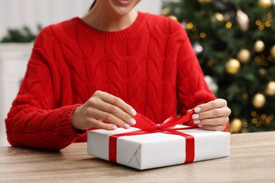 Photo of Woman opening Christmas gift at wooden table indoors, closeup