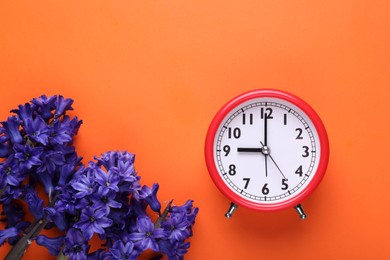 Photo of Red alarm clock and beautiful hyacinth flowers on orange background, flat lay. Spring time