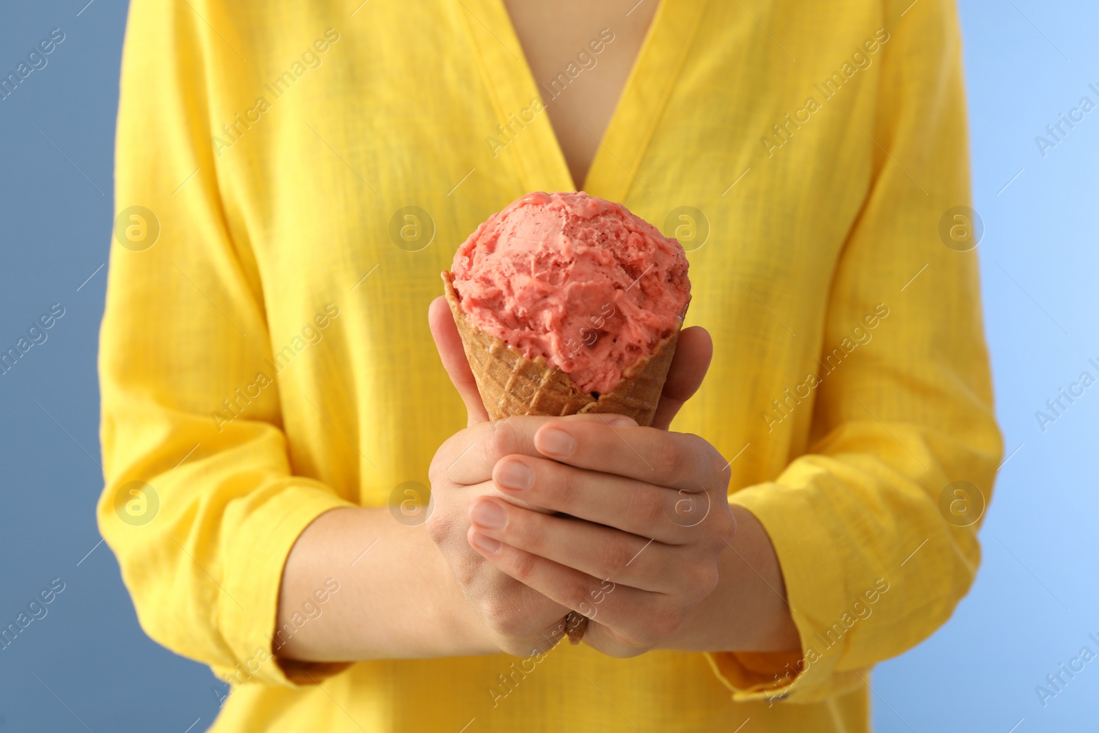 Photo of Woman holding pink ice cream in wafer cone on light blue background, closeup