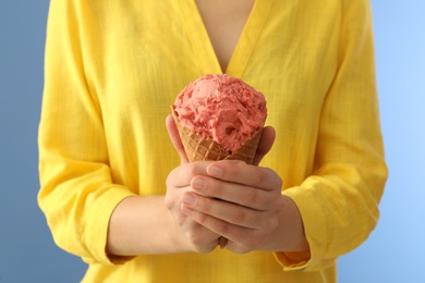 Photo of Woman holding pink ice cream in wafer cone on light blue background, closeup