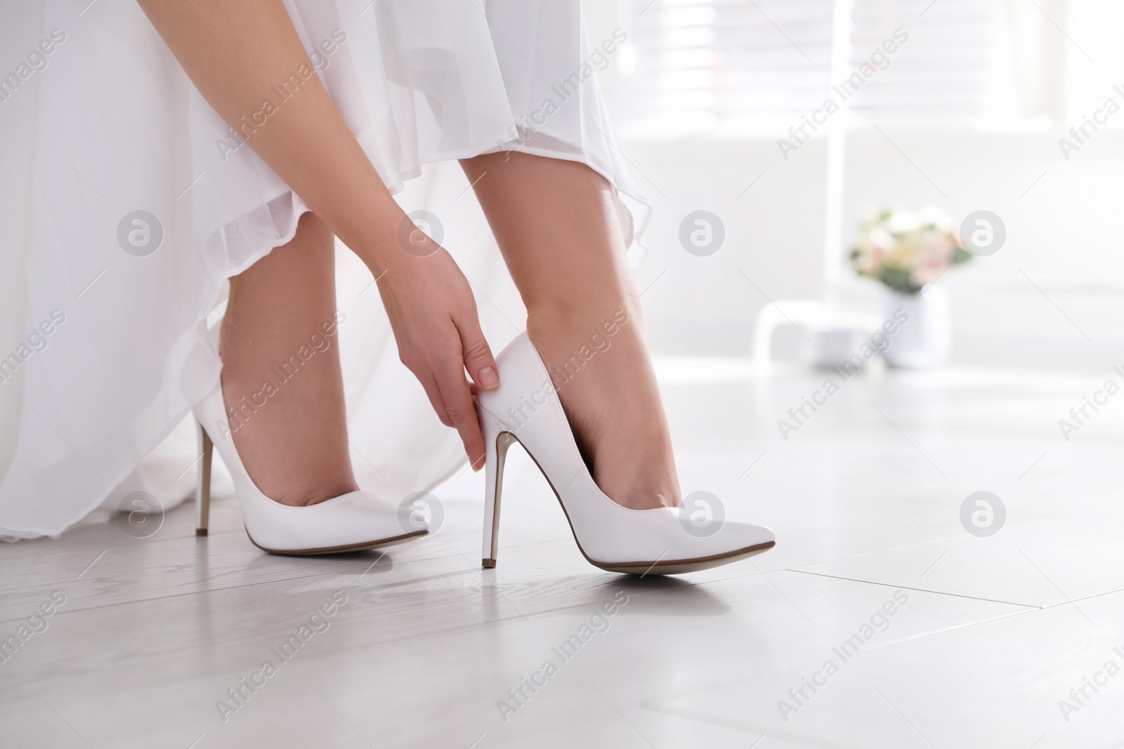 Photo of Young bride putting on beautiful wedding shoes indoors, closeup