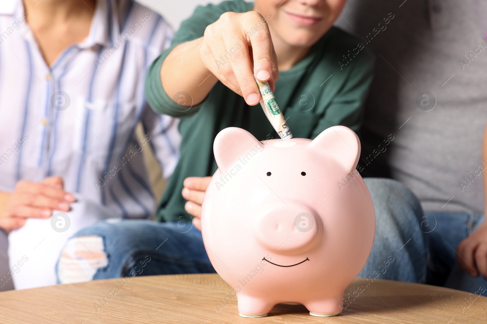 Photo of Boy with his mother putting money into piggy bank at home, closeup