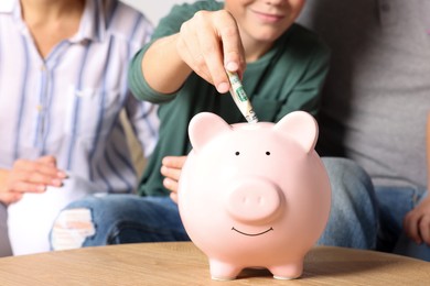 Boy with his mother putting money into piggy bank at home, closeup