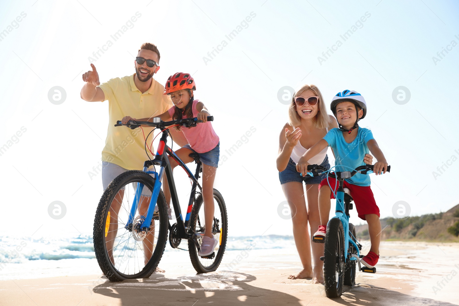 Photo of Happy parents teaching children to ride bicycles on sandy beach near sea