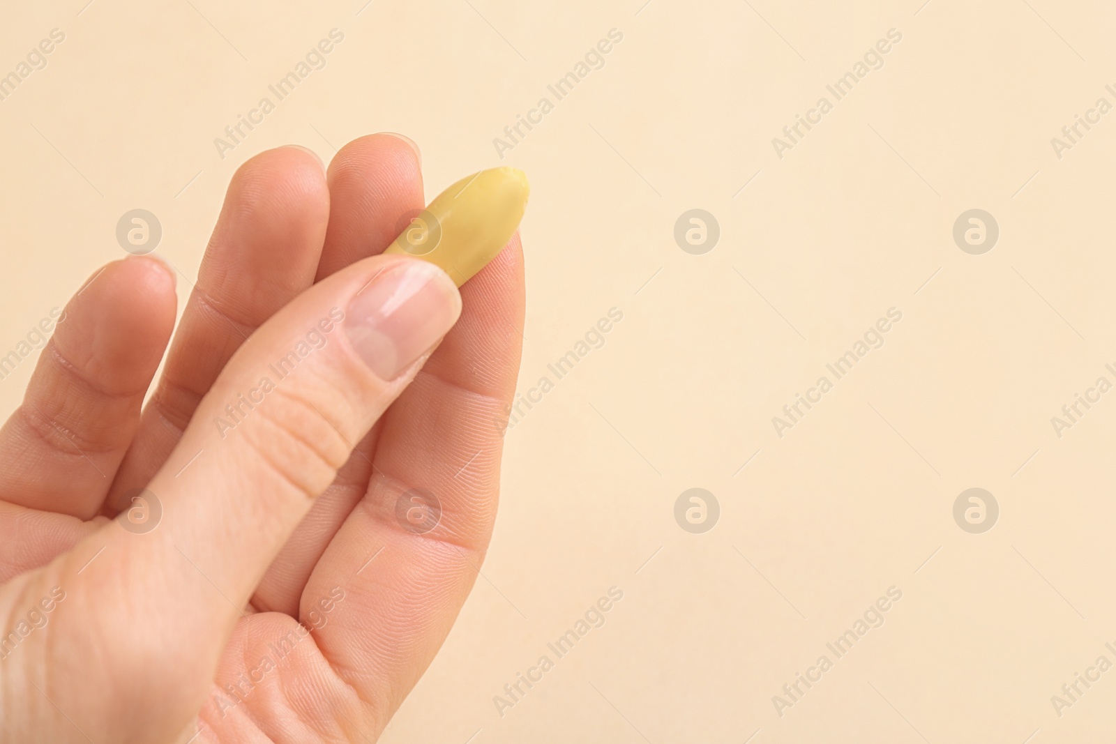 Photo of Closeup view of woman holding suppository on beige background, space for text. Hemorrhoid treatment