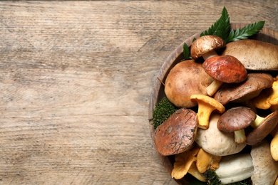 Photo of Bowl with different mushrooms on wooden table, top view. Space for text