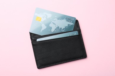 Leather card holder with credit cards on pink background, top view