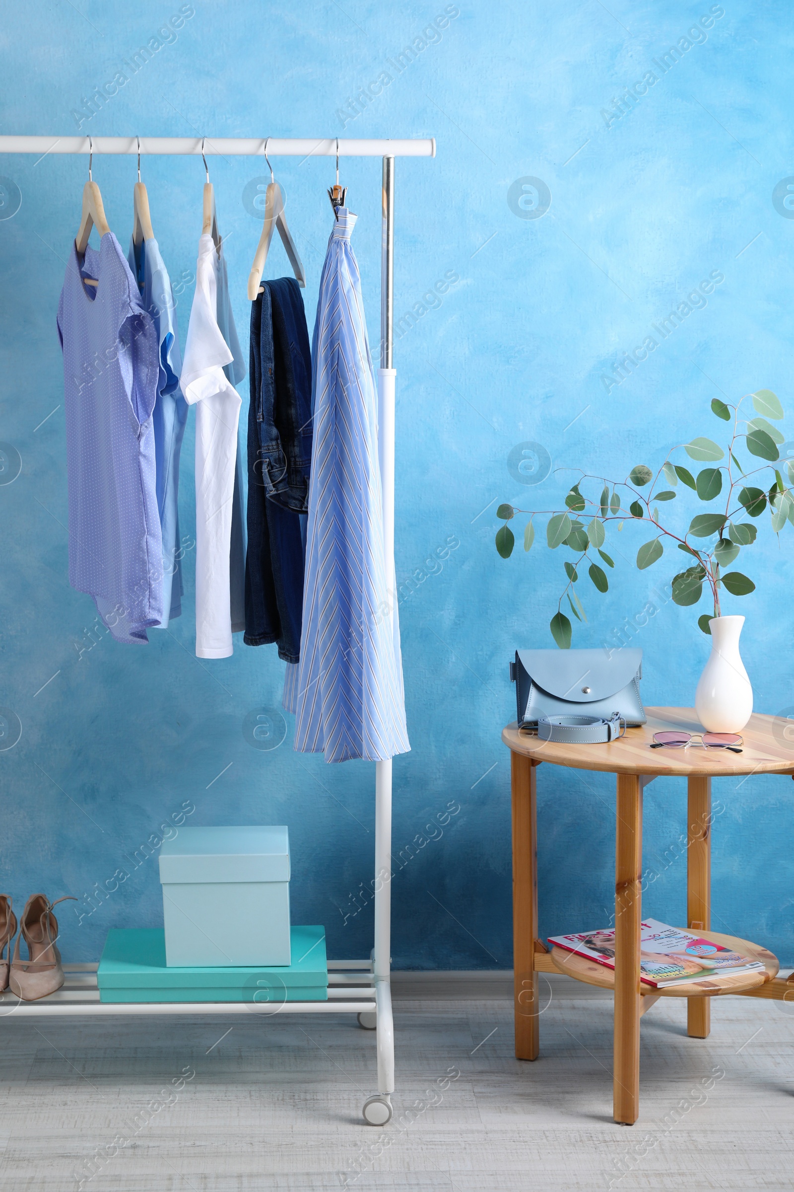 Photo of Rack with stylish clothes near light blue wall indoors