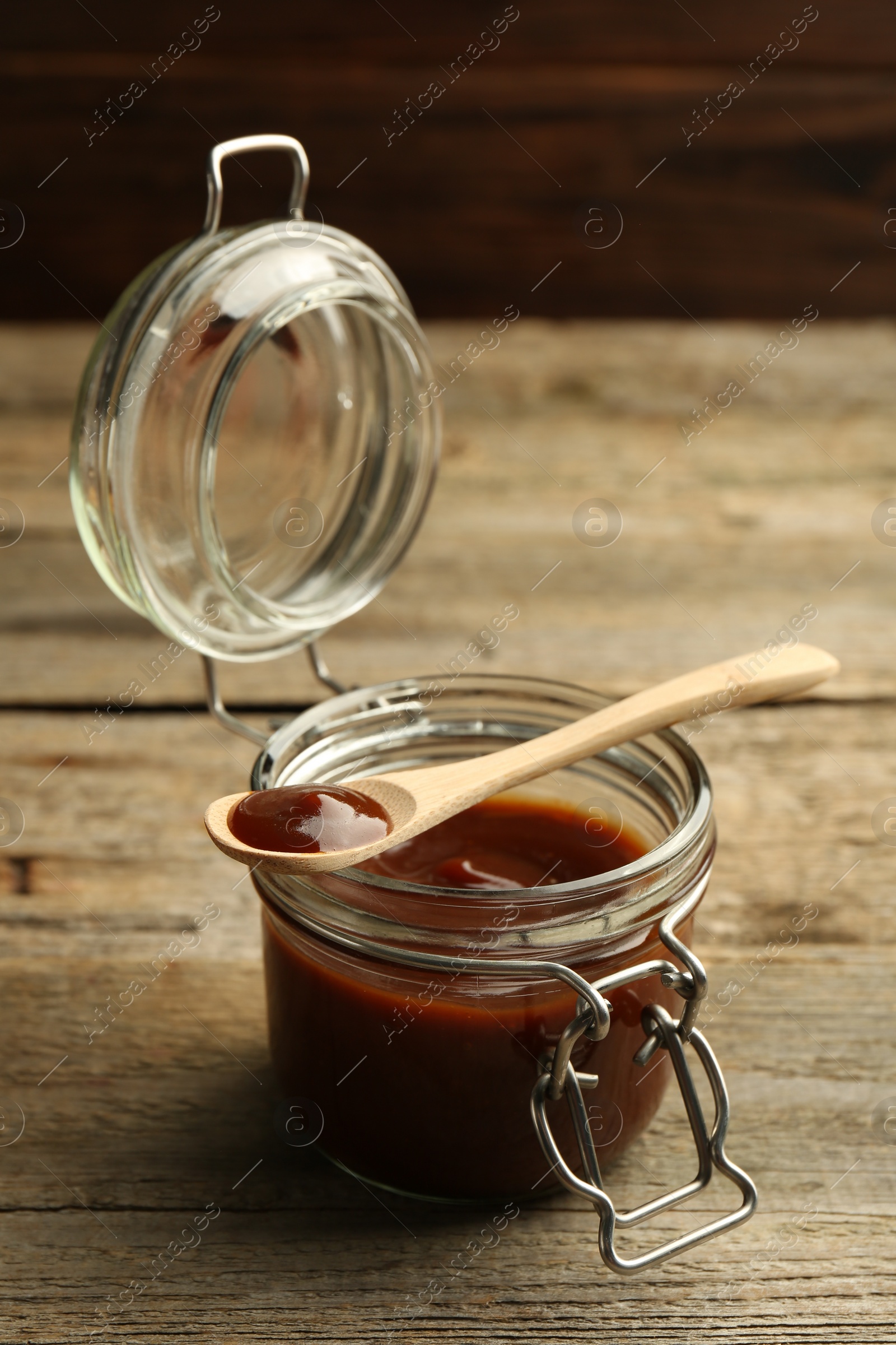 Photo of Tasty barbeque sauce in jar and spoon on wooden table