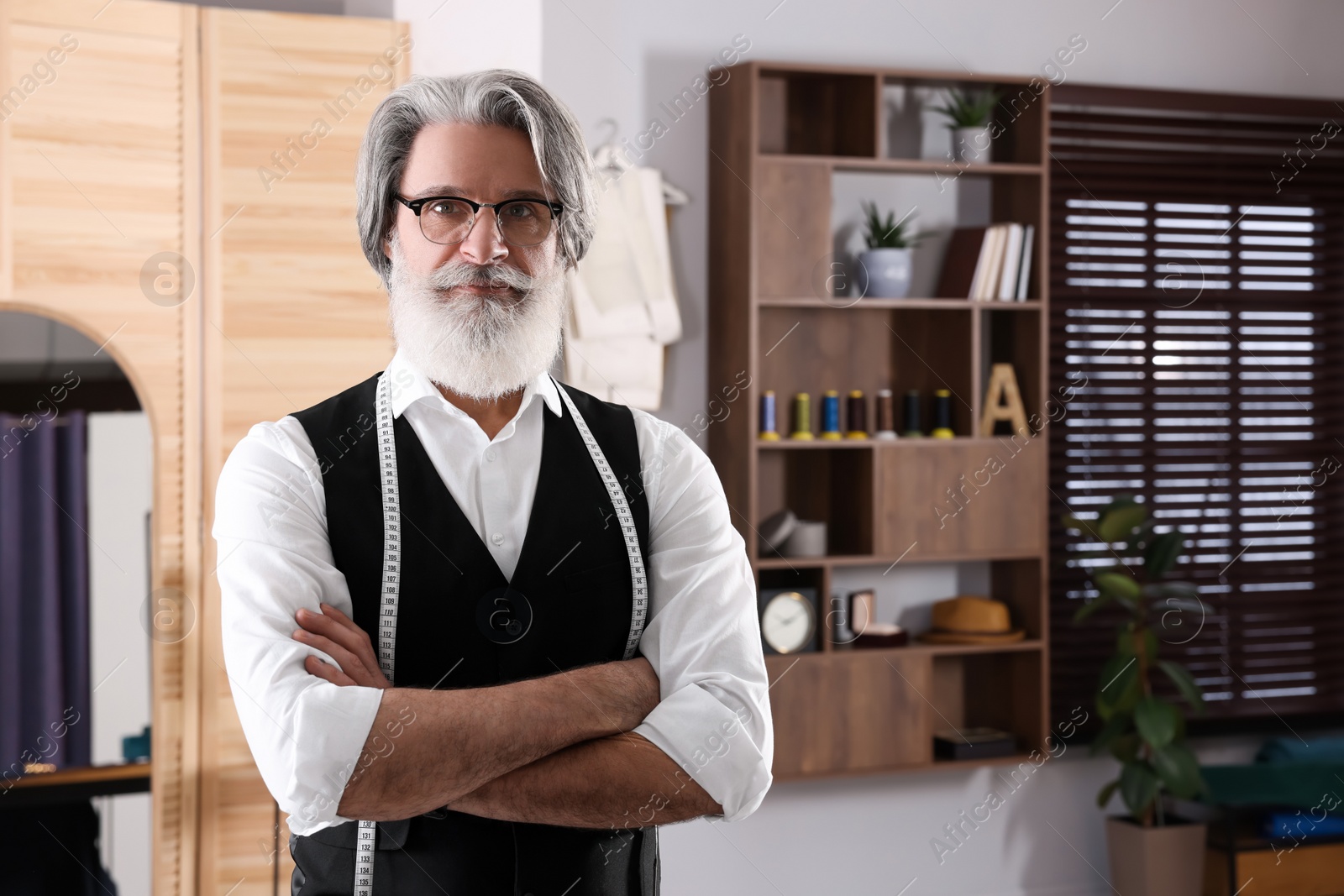 Photo of Professional tailor with measuring tape in workshop, space for text