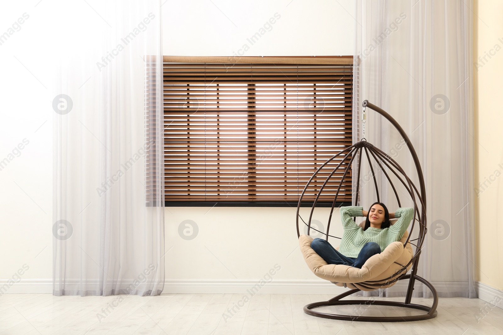 Photo of Young woman relaxing in hanging chair near window at home. Space for text