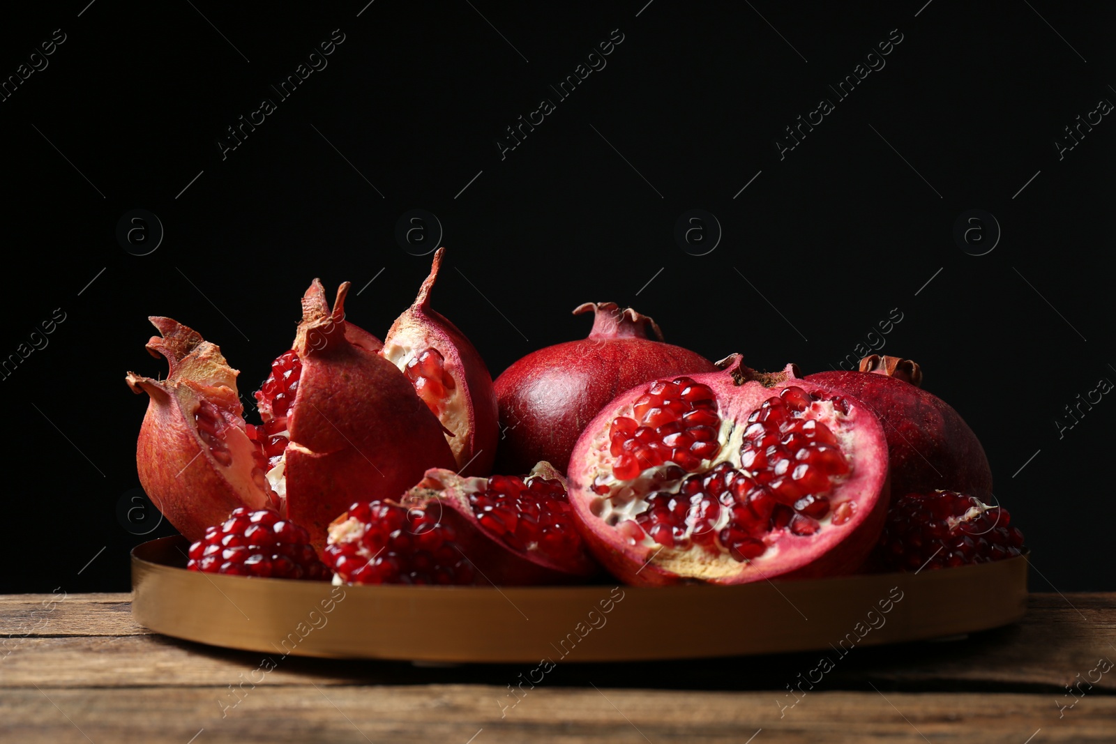 Photo of Tray with ripe pomegranates on table against black background