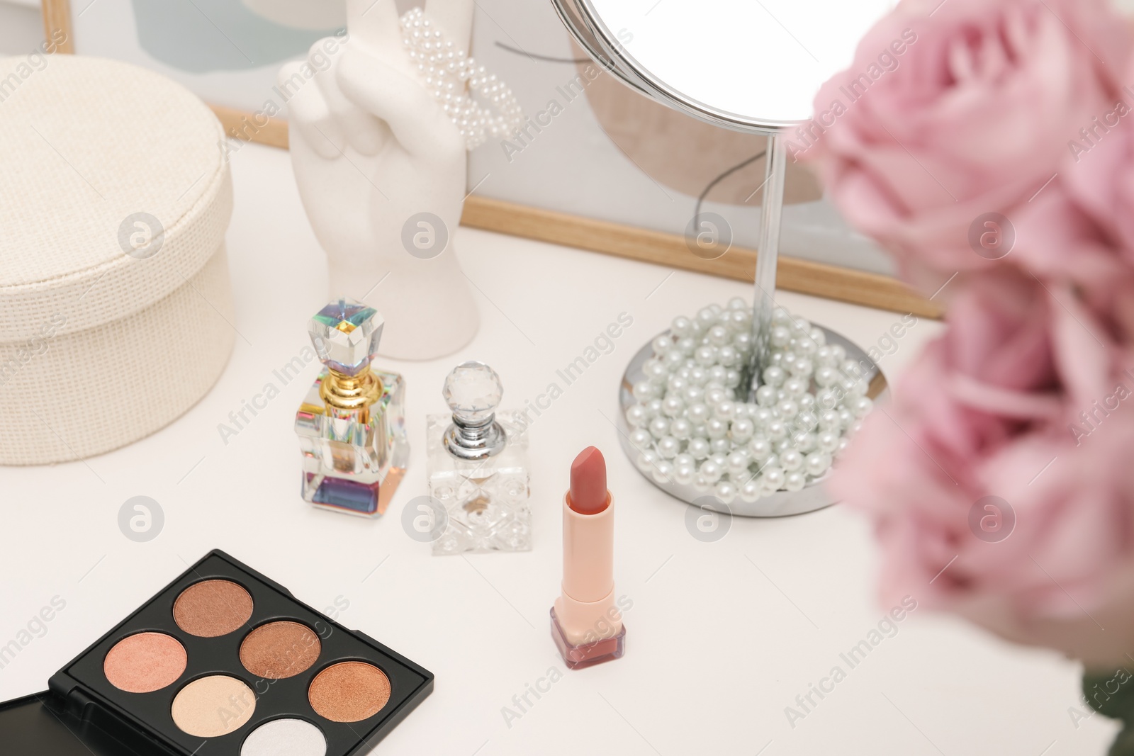 Photo of Mirror, cosmetic products, jewelry, perfumes and pink roses on white dressing table