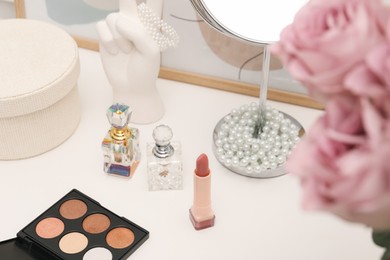 Mirror, cosmetic products, jewelry, perfumes and pink roses on white dressing table