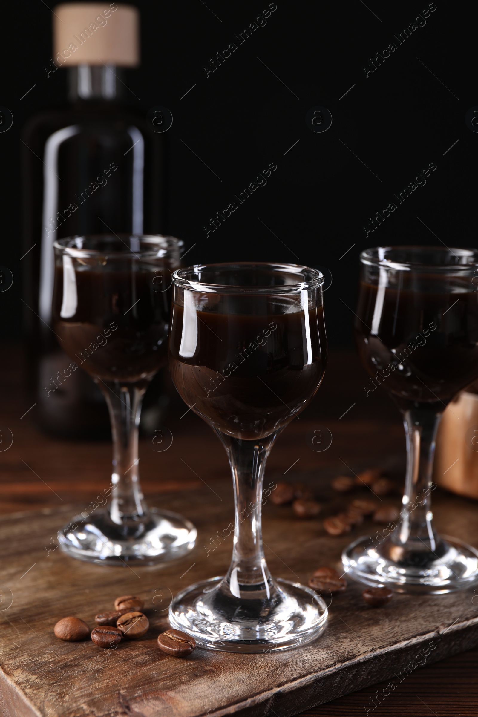 Photo of Shot glasses with coffee liqueur and beans on wooden table, closeup