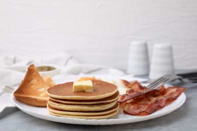 Tasty pancakes served with bacon on grey table