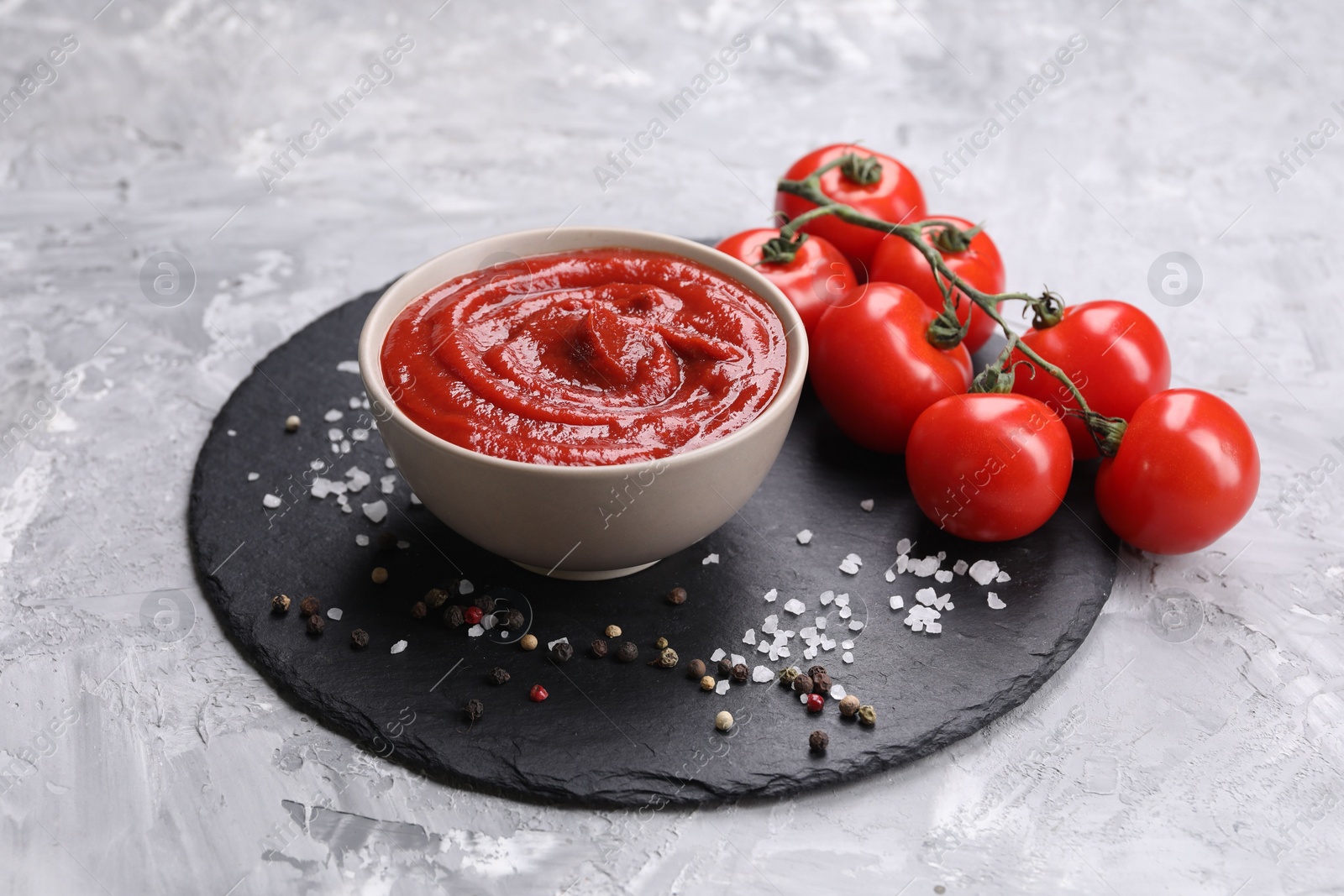 Photo of Organic ketchup in bowl, fresh tomatoes and spices on grey textured table. Tomato sauce