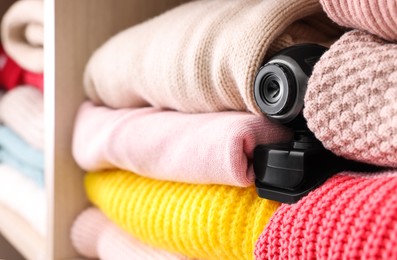 Photo of Camera hidden between clothes in wardrobe closet, closeup. Space for text