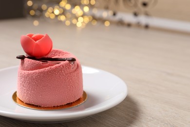 Photo of Delicious mousse cake with floral decor on white wooden table against blurred lights, closeup. Space for text