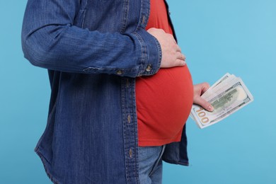 Photo of Surrogate mother. Pregnant woman with dollar banknotes on light blue background, closeup