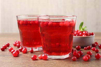 Photo of Tasty cranberry juice in glasses and fresh berries on wooden table, closeup