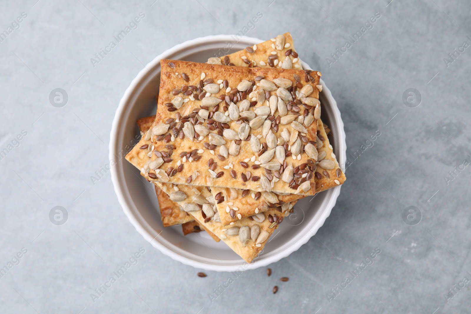 Photo of Cereal crackers with flax, sunflower and sesame seeds in bowl on grey table, top view