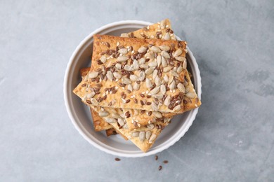 Photo of Cereal crackers with flax, sunflower and sesame seeds in bowl on grey table, top view