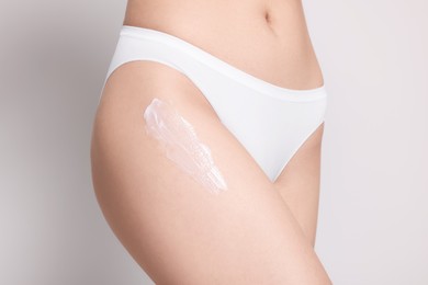 Woman with body cream smear on hip against light grey background, closeup