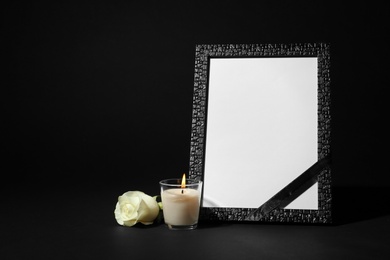 Photo of Funeral photo frame with ribbon, white rose and candle on black background. Space for design