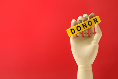 Photo of Mannequin hand holding word Donor made of cubes on red background. Space for text