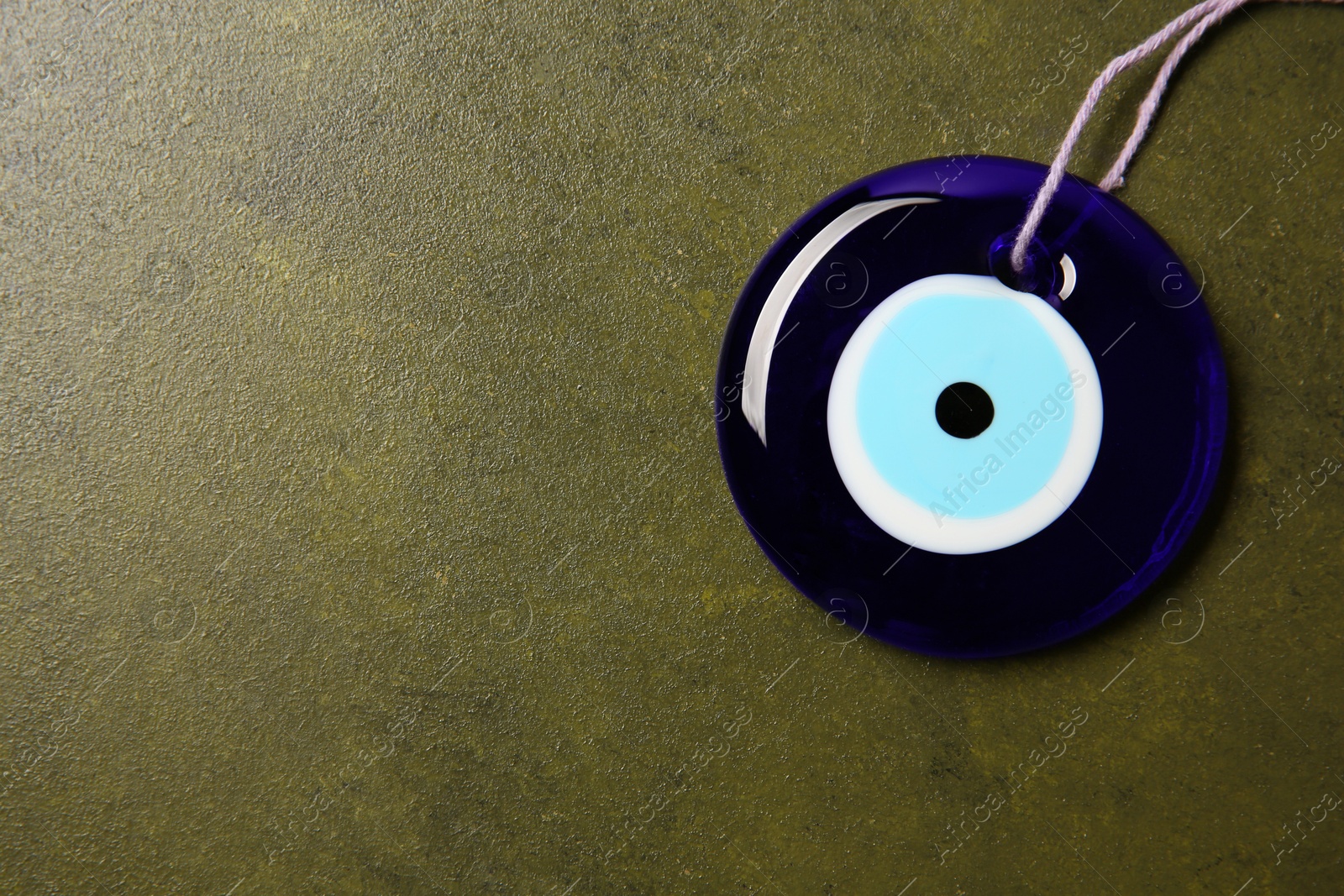 Photo of Evil eye amulet on olive textured table, top view. Space for text
