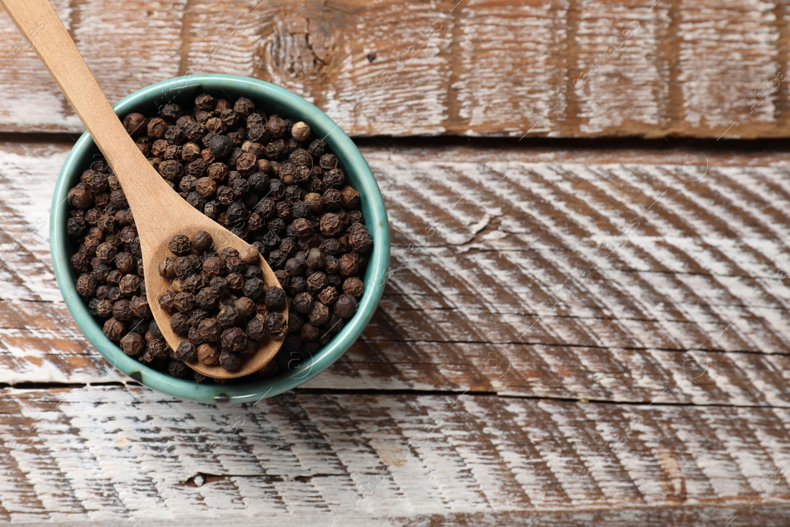 Photo of Aromatic spice. Black pepper in bowl and spoon on wooden table, top view. Space for text