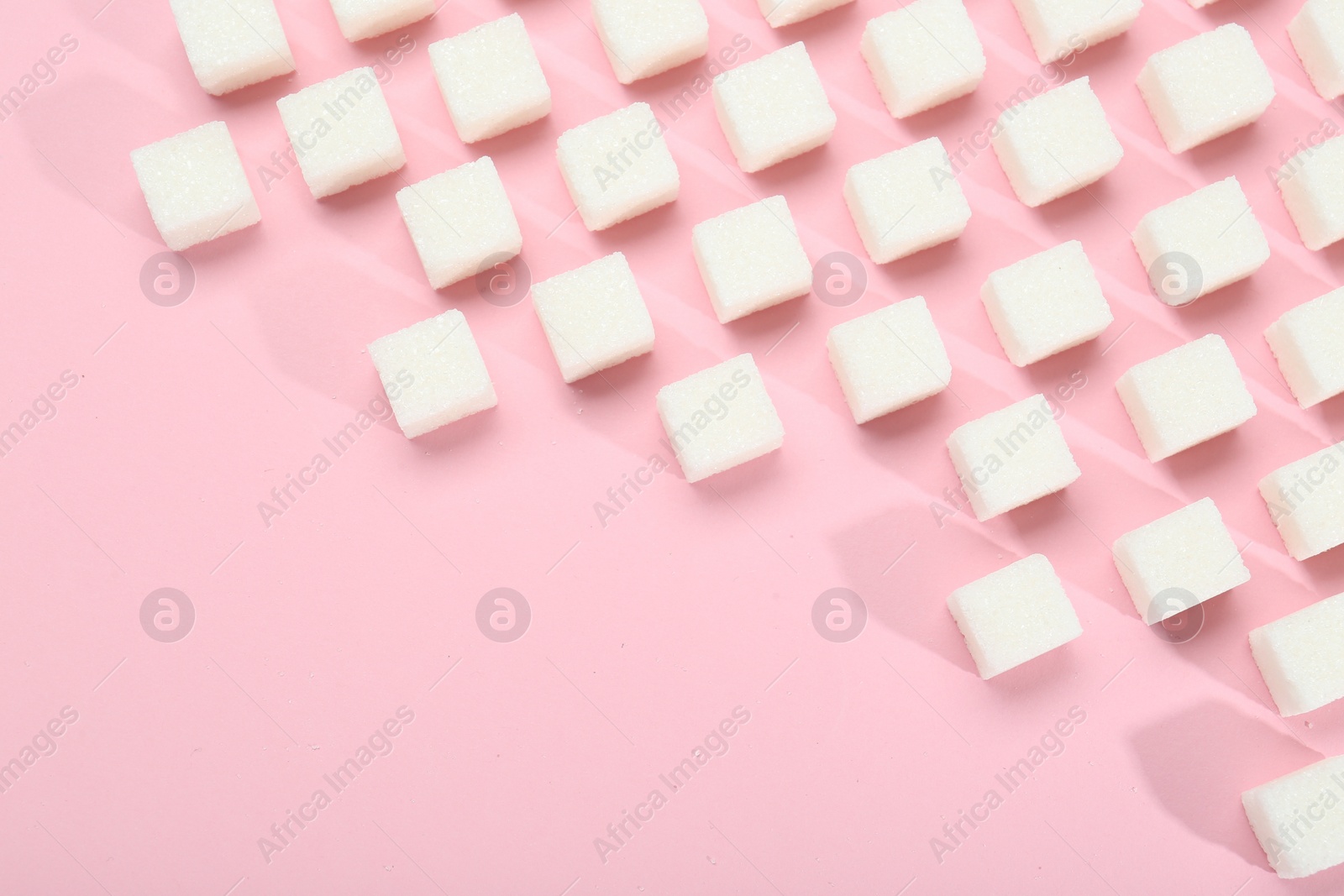 Photo of White sugar cubes on pink background, top view. Space for text