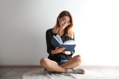 Photo of Young woman reading book on floor near wall