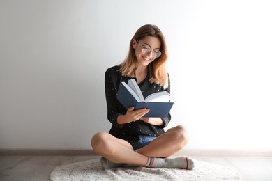 Young woman reading book on floor near wall