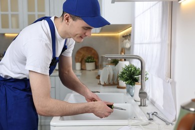 Smiling plumber repairing sink with screwdriver in kitchen