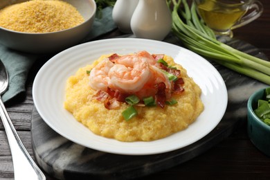 Photo of Plate with fresh tasty shrimps, bacon, grits and green onion on dark wooden table