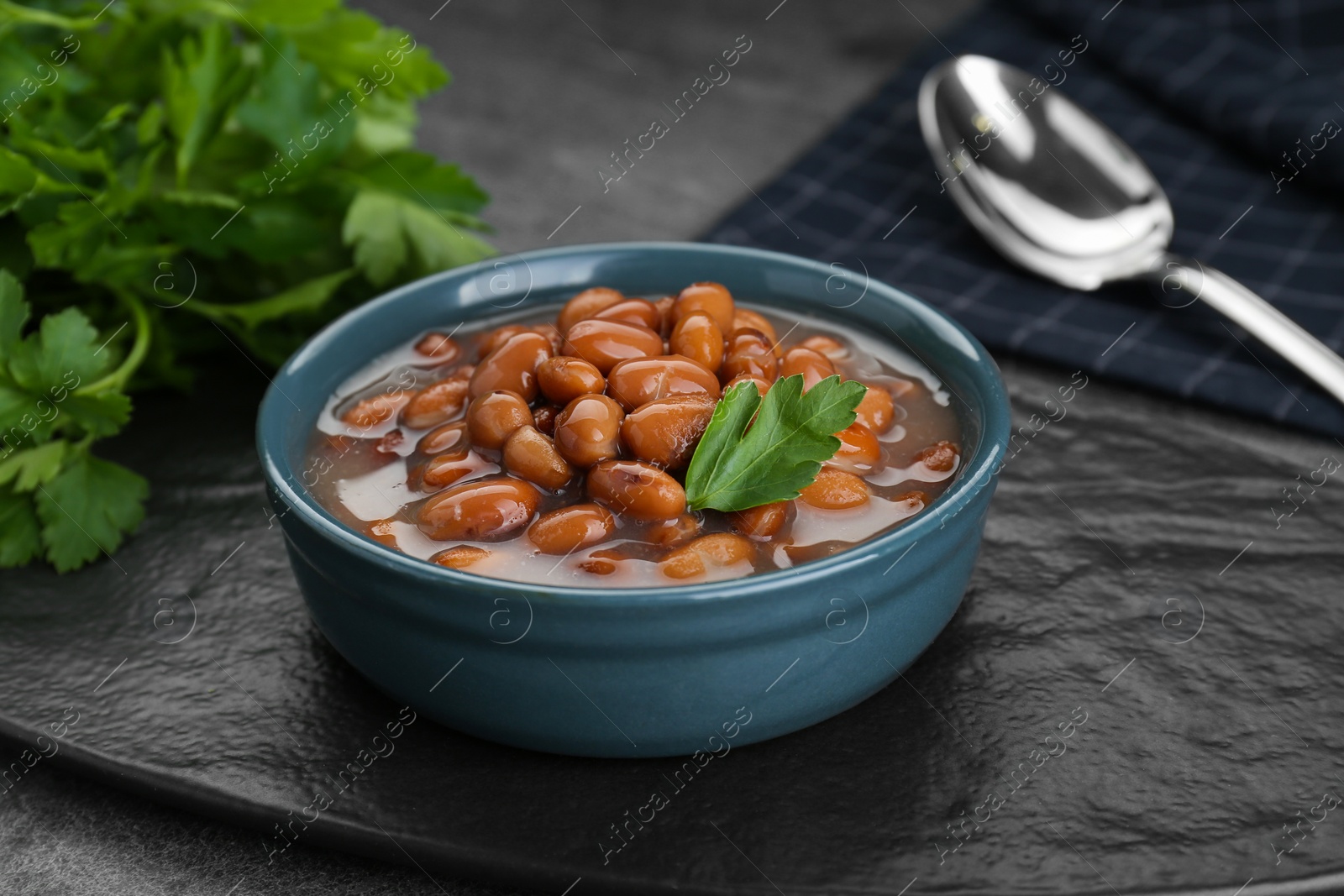 Photo of Bowl of canned kidney beans with parsley on grey table, closeup