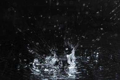 Photo of Rain drop falling down into puddle on dark background