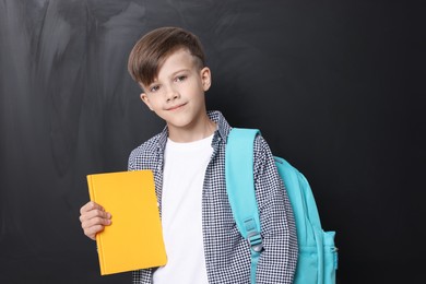 Photo of Back to school. Cute boy holding book near chalkboard