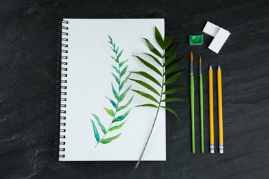 Photo of Painting of green twig in sketchbook and art supplies on black table, flat lay
