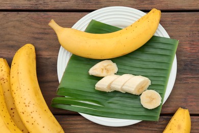 Photo of Delicious ripe bananas and fresh leaf on wooden table, above view