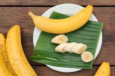 Delicious ripe bananas and fresh leaf on wooden table, above view