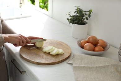 Photo of Woman cutting white onion into rings at countertop, closeup