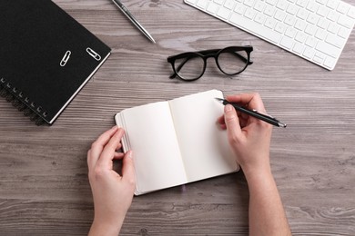 Photo of Woman writing in notebook at wooden table, top view